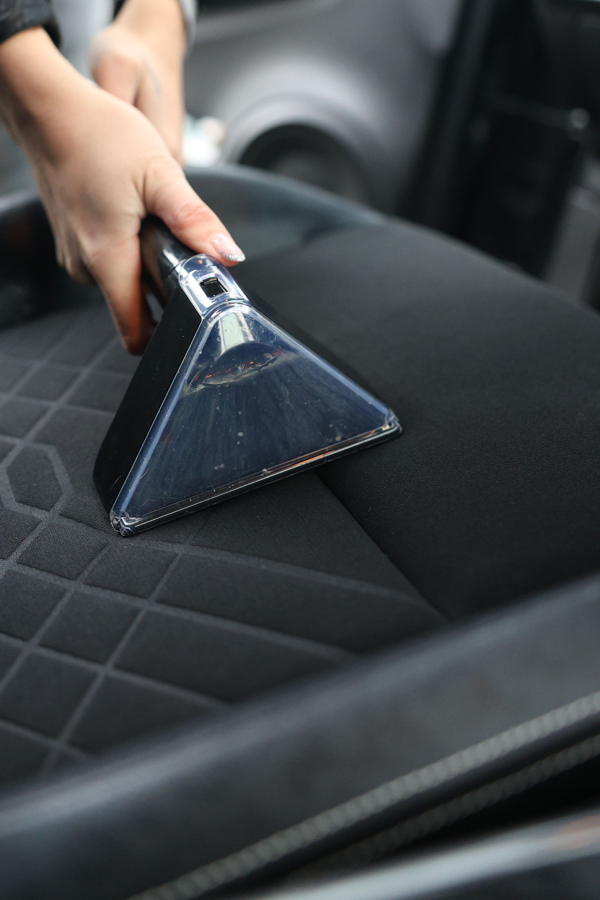 Young girl cleaning of car interior by wet-dry vacuum machine