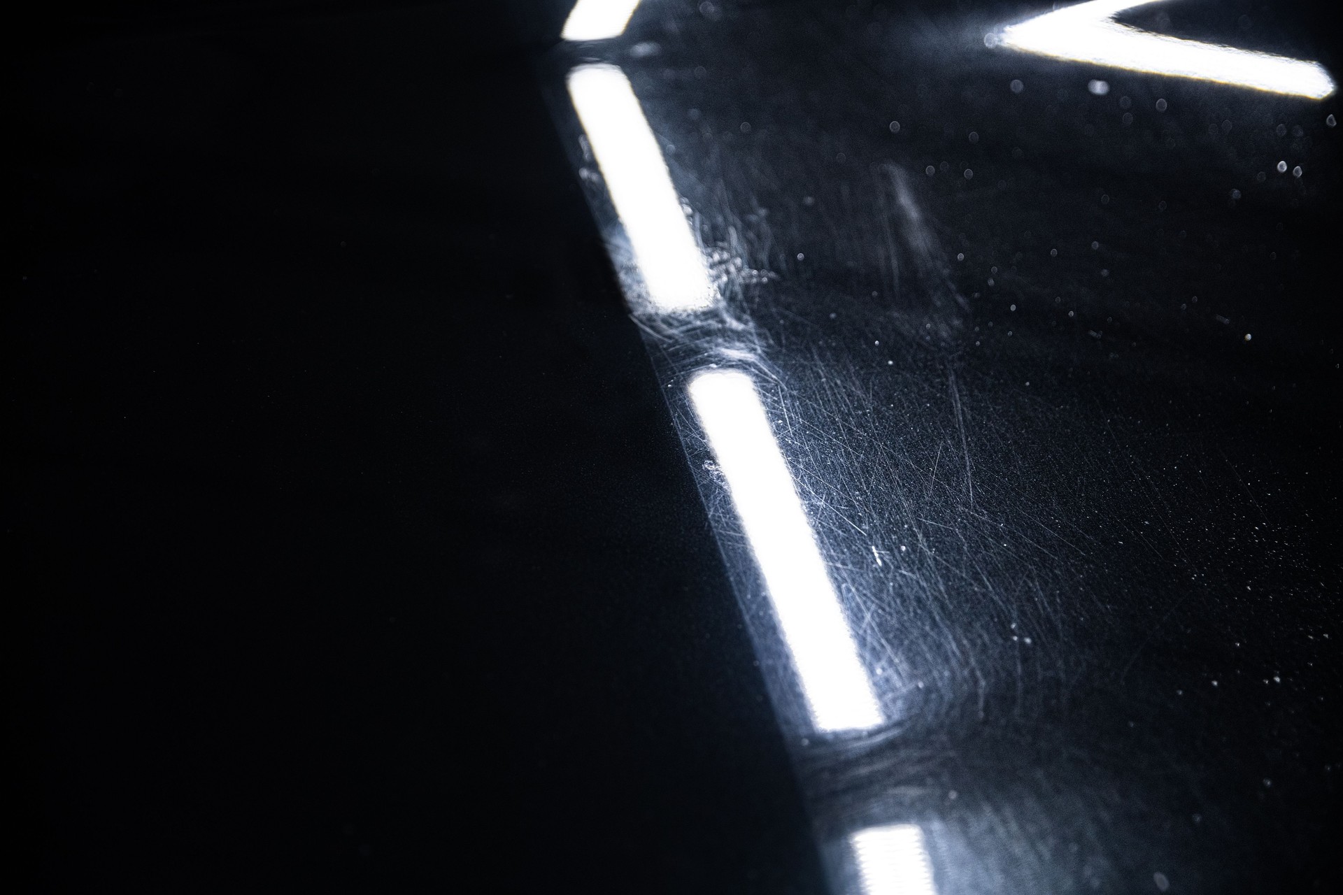 Before and after effect of a paint correction on the paintwork of a black car in a car detailing studio.